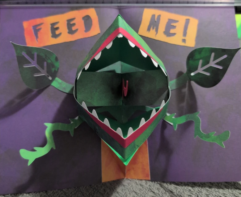 Pop-up book of a man-eating plant with lips and teeth and tentacle-like vines.