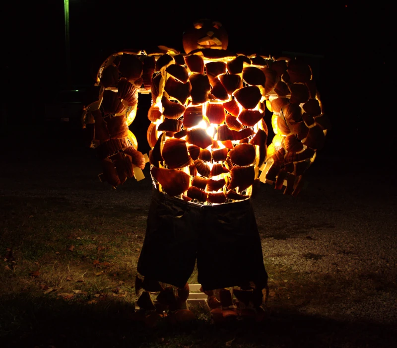 The Thing made out of pumpkins, standing outside in the dark, lit by a light bulb in its chest.